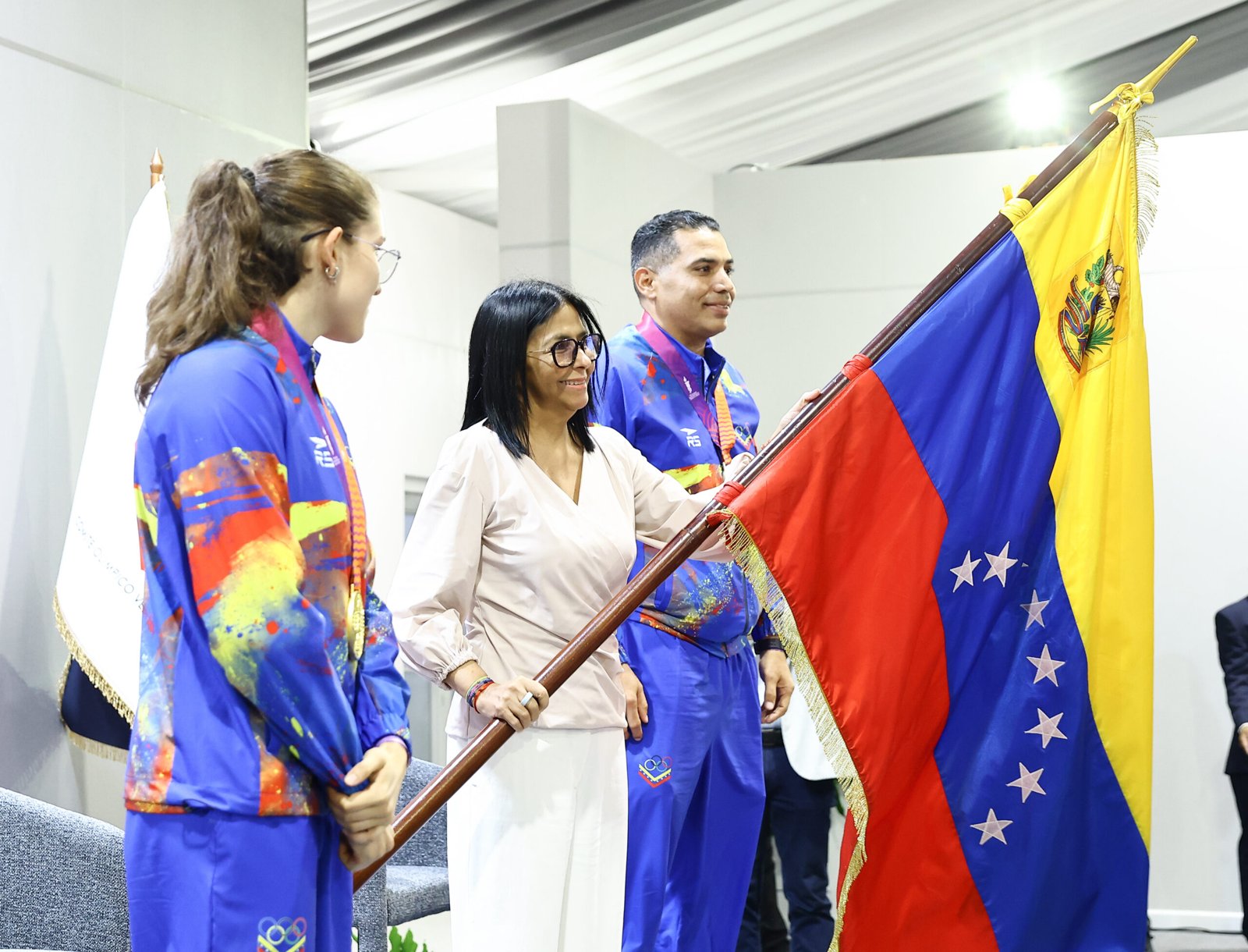 Delcy Rodríguez sostiene la bandera de Venezuela junto a dos atletas de la delegación de Santa Fe 2026