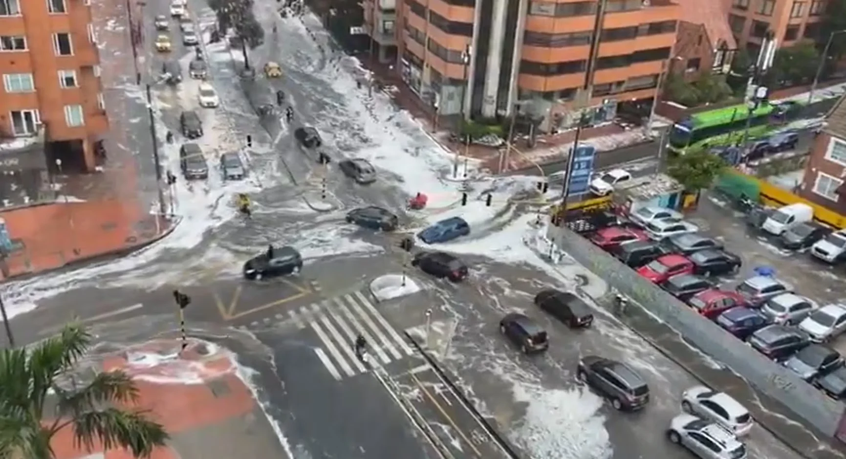 Vista desde lo alto de un cruce de avenidas en Bogotá, con calzadas y aceras cubiertas de granizo y carros circulando