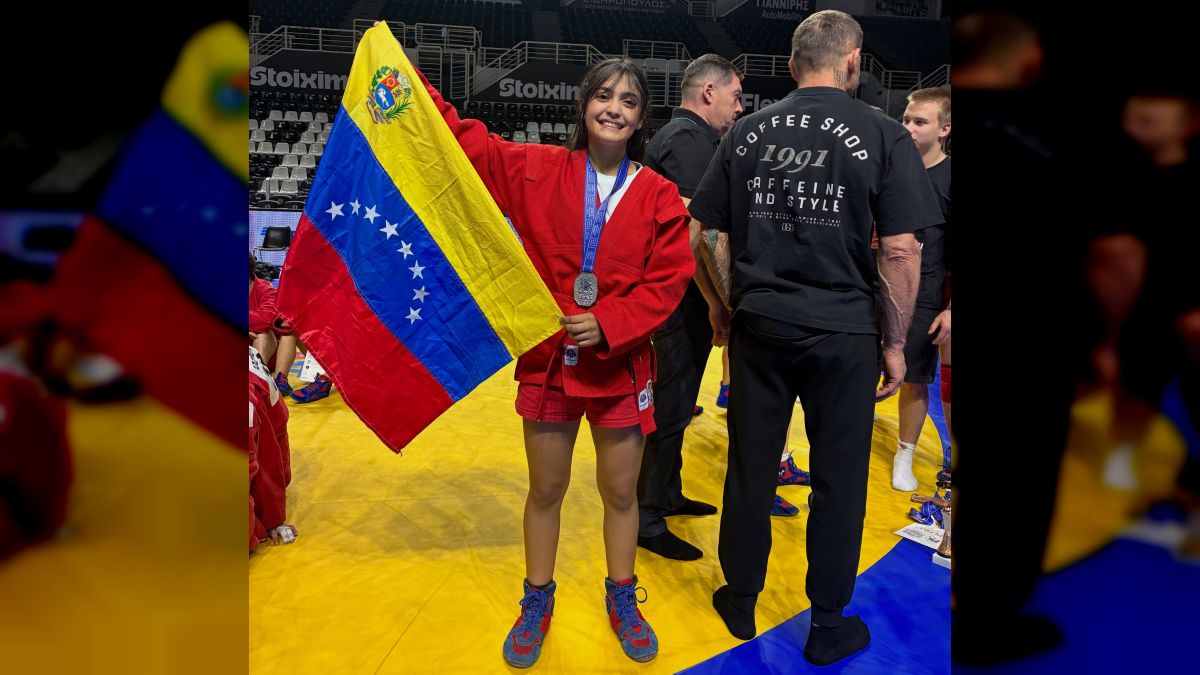 Una sambista con uniforme rojo sostiene la bandera de Venezuela y lleva una medalla de plata al cuello