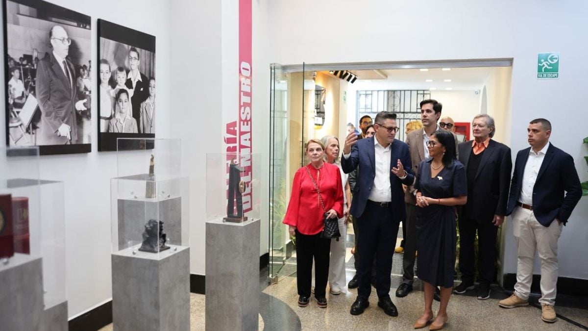 Un grupo de personas recorre una sala de exposición con fotografías en blanco y negro en la pared y vitrinas con objetos
