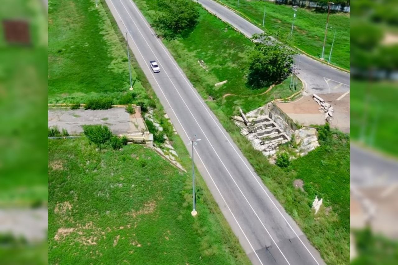Vista aérea de una carretera de dos vías entre áreas verdes, con un tramo de concreto roto y escombros a un costado