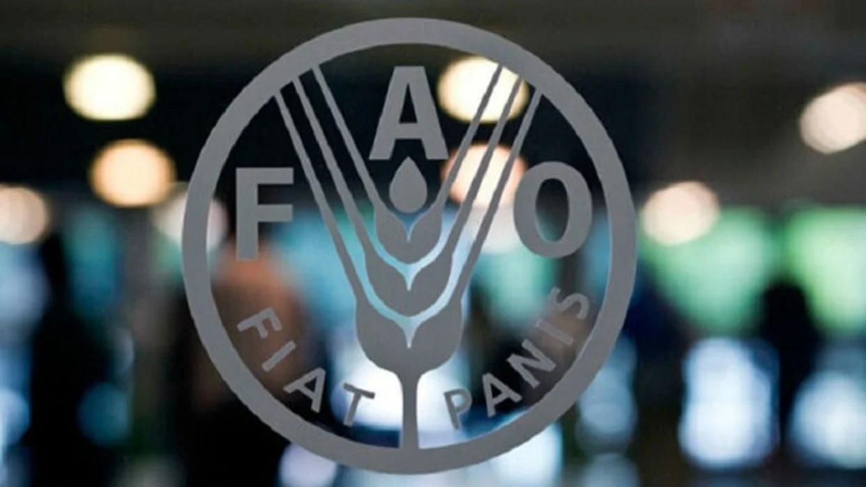 El logo de la FAO, con una espiga y el lema «Fiat panis», sobre un fondo desenfocado