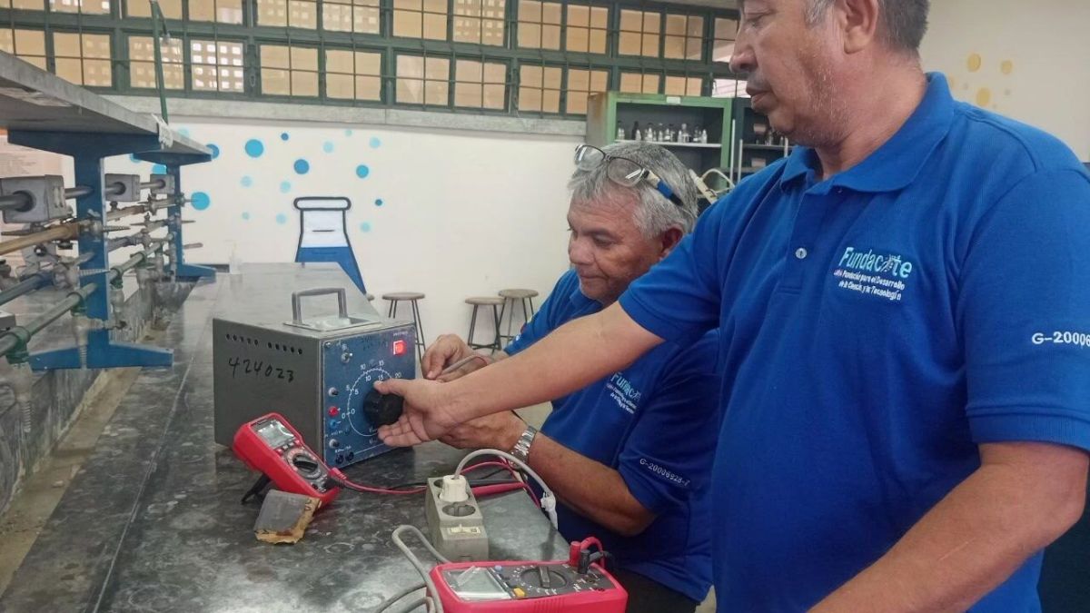 Dos técnicos con franelas de Fundacite revisan una fuente de poder con multímetros sobre el mesón de un laboratorio