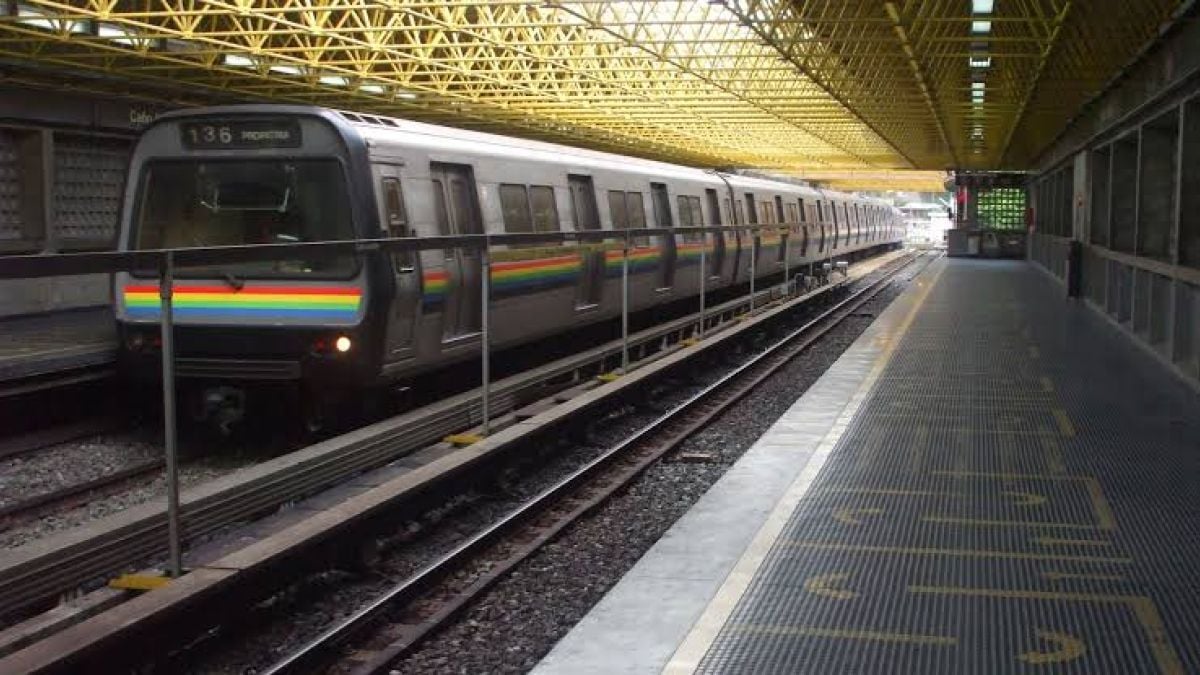 Un tren del Metro de Caracas, con franjas de colores en el frente, detenido junto a un andén vacío bajo un techo de estructura amarilla