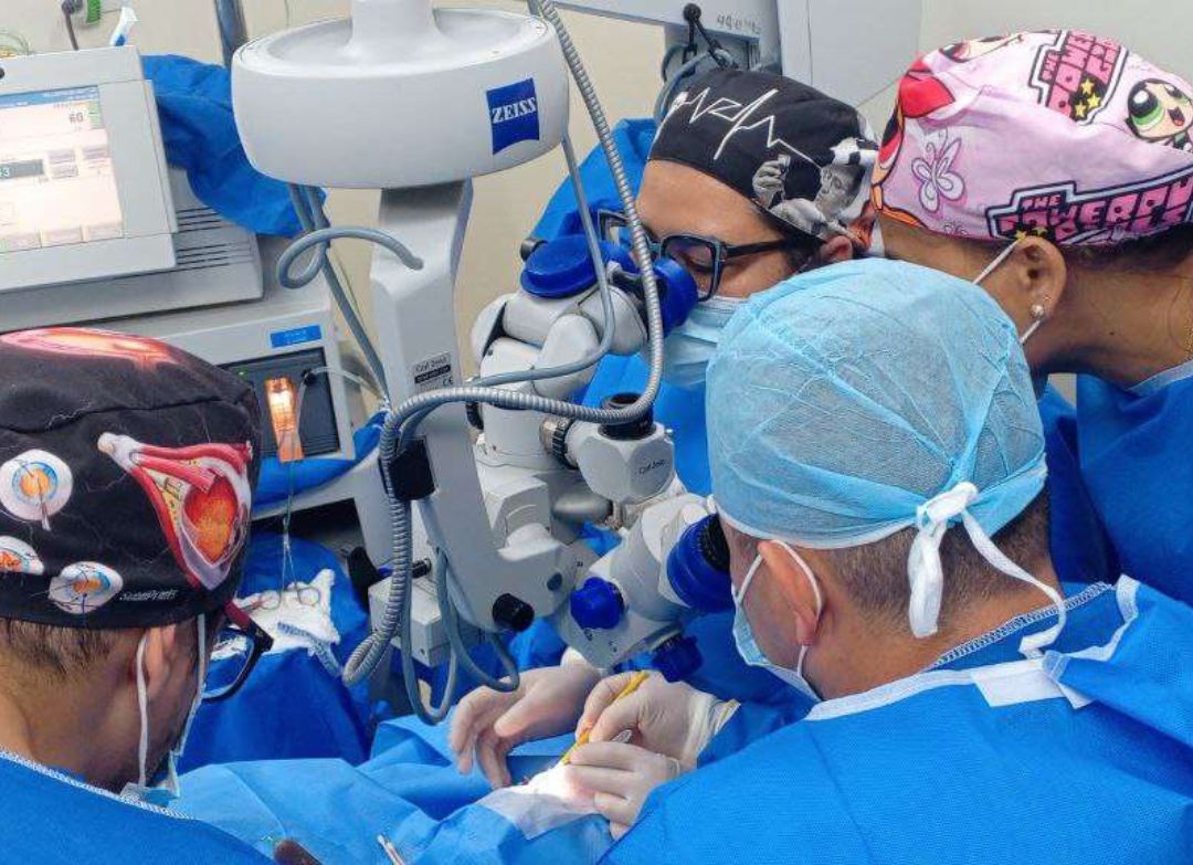 Un equipo médico con gorros quirúrgicos y mascarillas opera con un microscopio quirúrgico en un quirófano