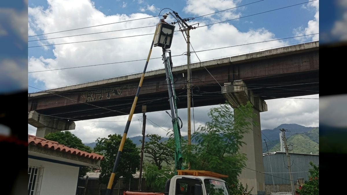 Un trabajador de Corpoelec repara una línea eléctrica desde una cesta elevada, bajo un viaducto