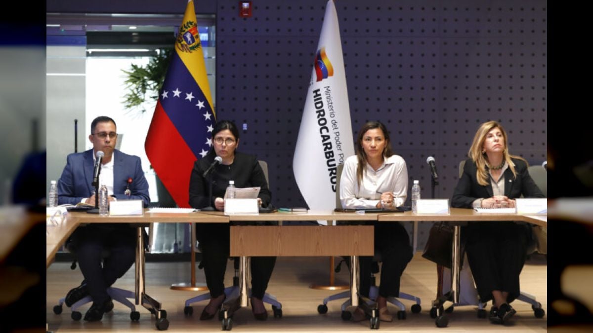 Cuatro personas sentadas en una mesa de trabajo con micrófonos, frente a una bandera de Venezuela y otra del Ministerio de Hidrocarburos