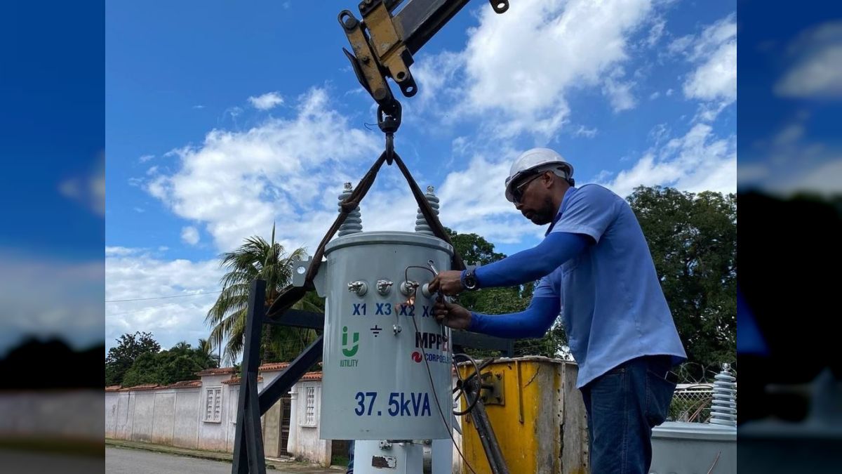 Un trabajador de Corpoelec con casco revisa un transformador de 37,5 kVA suspendido de una grúa