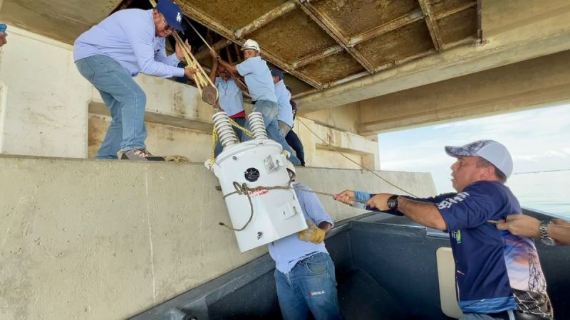 Trabajadores de Corpoelec bajan un transformador desde una lancha bajo el Puente sobre el Lago de Maracaibo