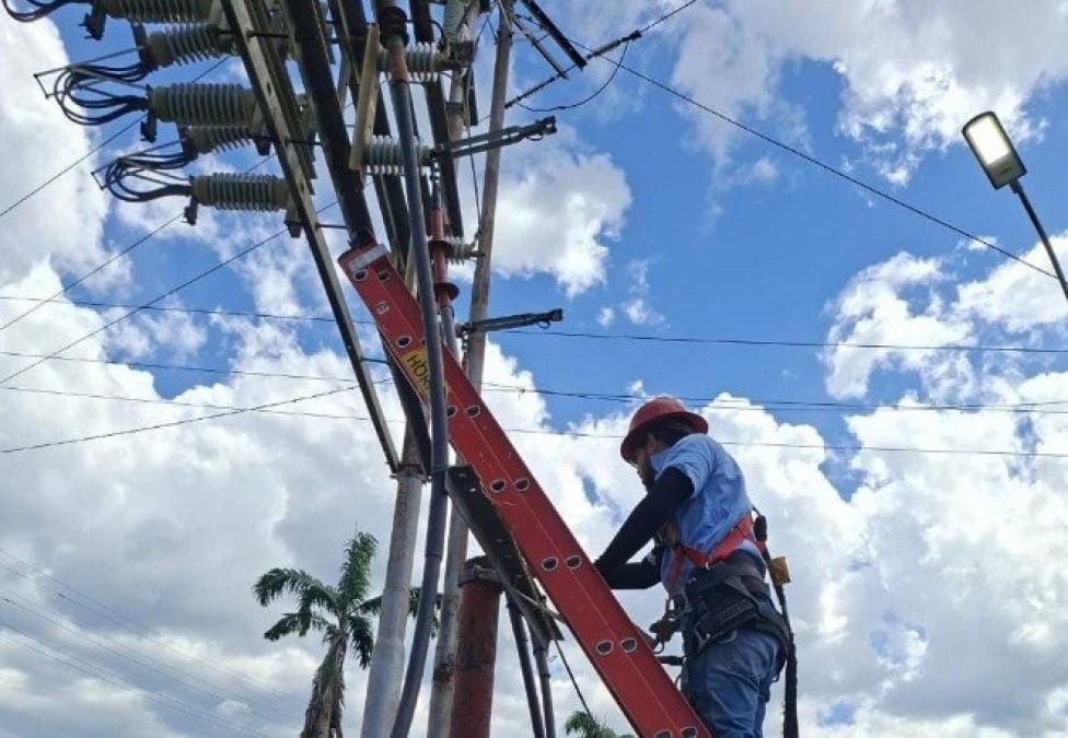 Un trabajador de Corpoelec con casco sube por una escalera a una estructura eléctrica