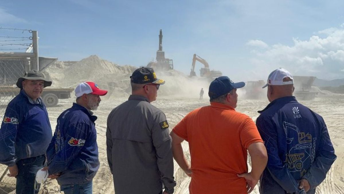Cinco hombres observan a máquinas cargando arcilla blanca en una cantera