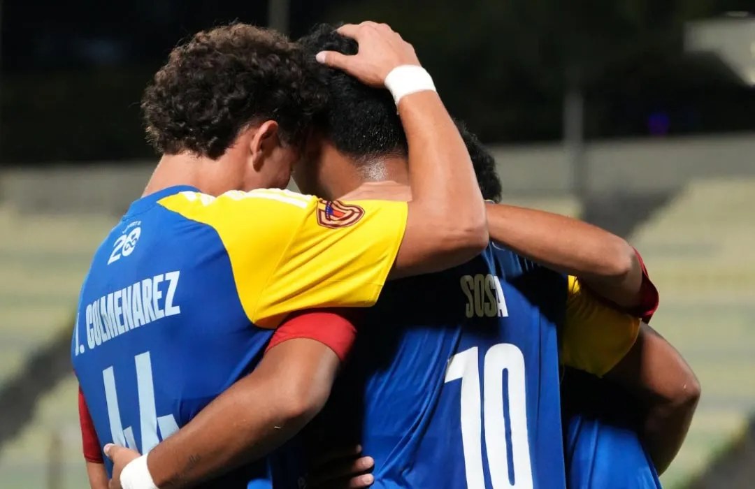 Tres futbolistas con camisetas azules y amarillas se abrazan de espaldas en un estadio