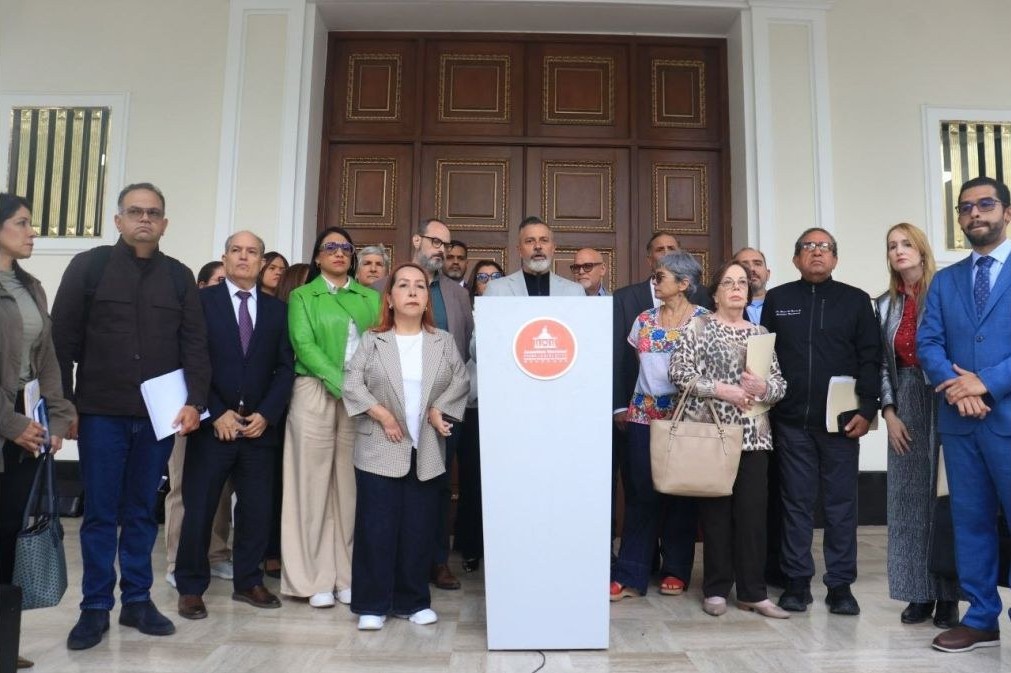 Un grupo de personas posa de pie detrás de un atril, frente a una gran puerta de madera