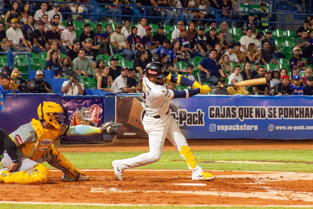 Un bateador de los Tigres de Aragua hace swing ante el receptor, con el público en las tribunas