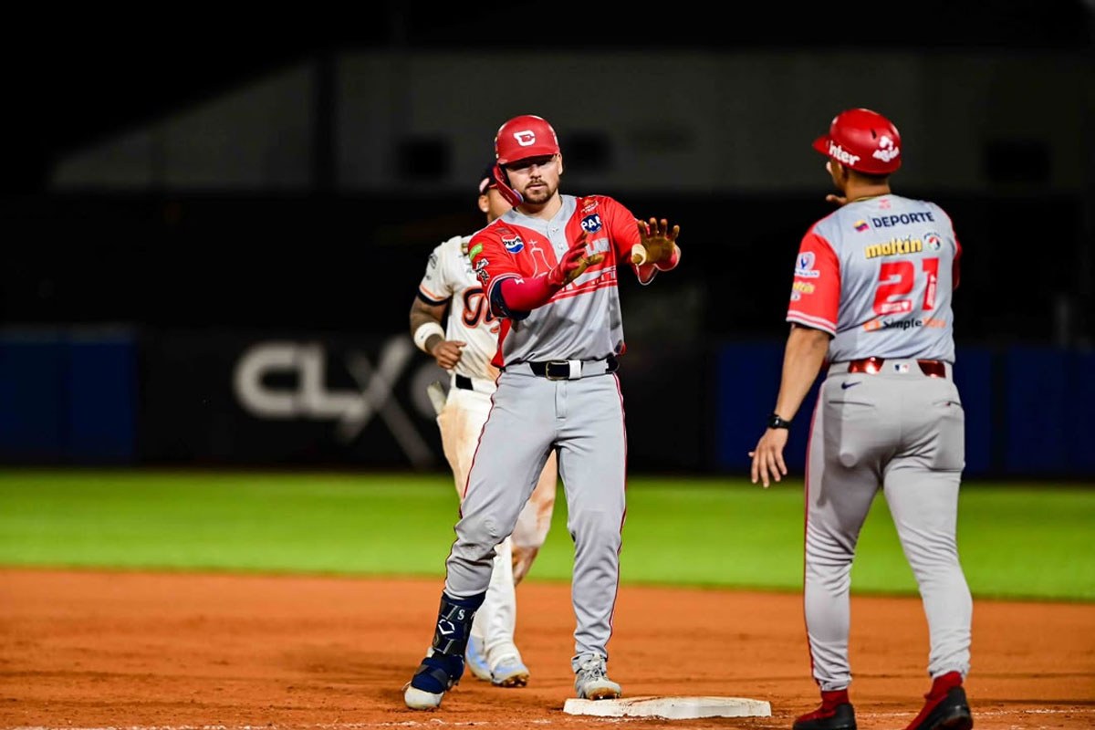 Un pelotero en primera base conversa con su coach durante un juego de béisbol