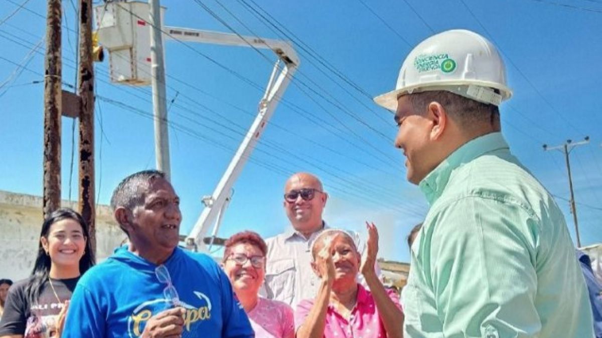Un funcionario con casco conversa con vecinos junto a un camión con grúa en una calle