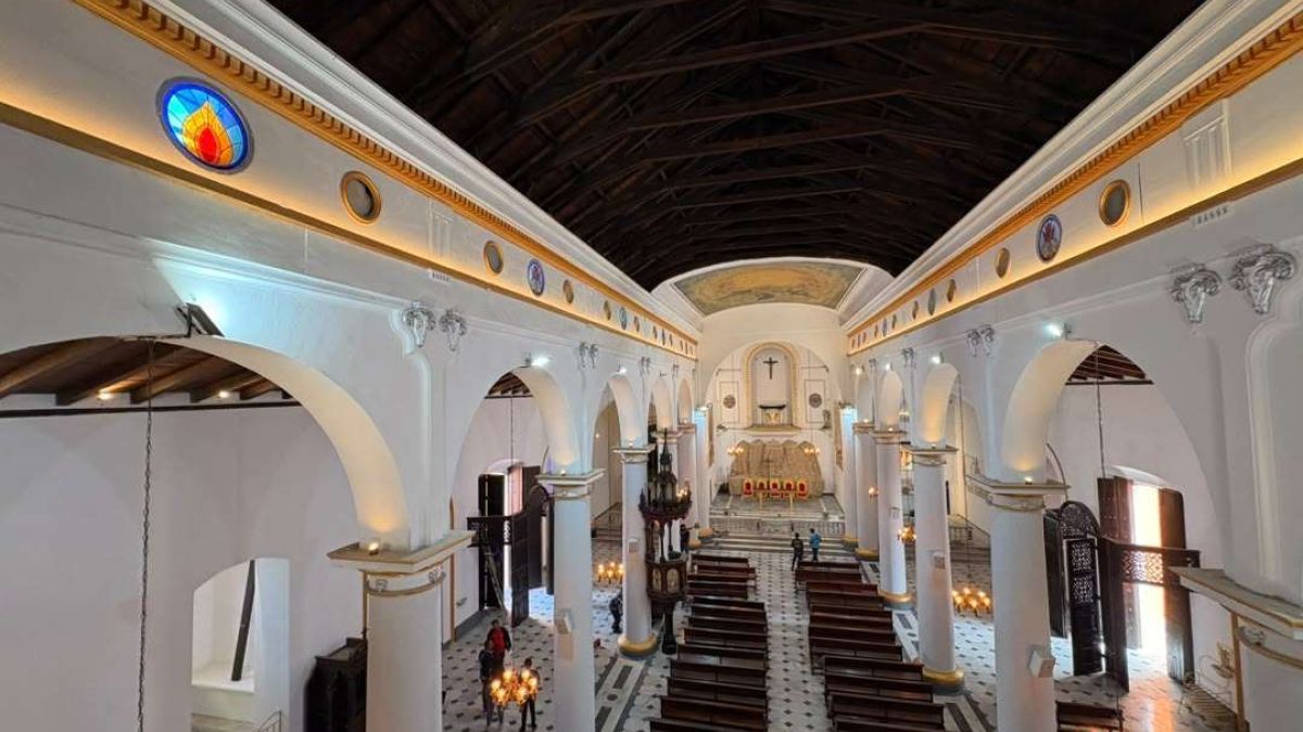 Interior de una iglesia con columnas blancas, arcos y bancos de madera