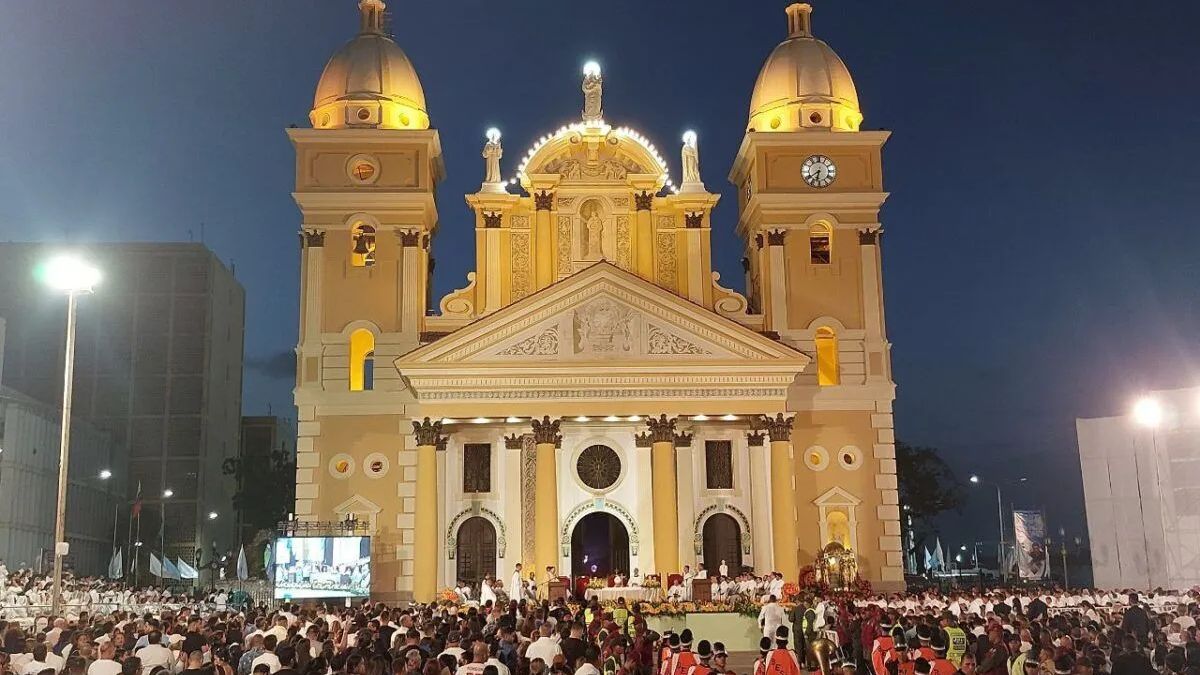 Fachada iluminada de una basílica de noche con una multitud al frente