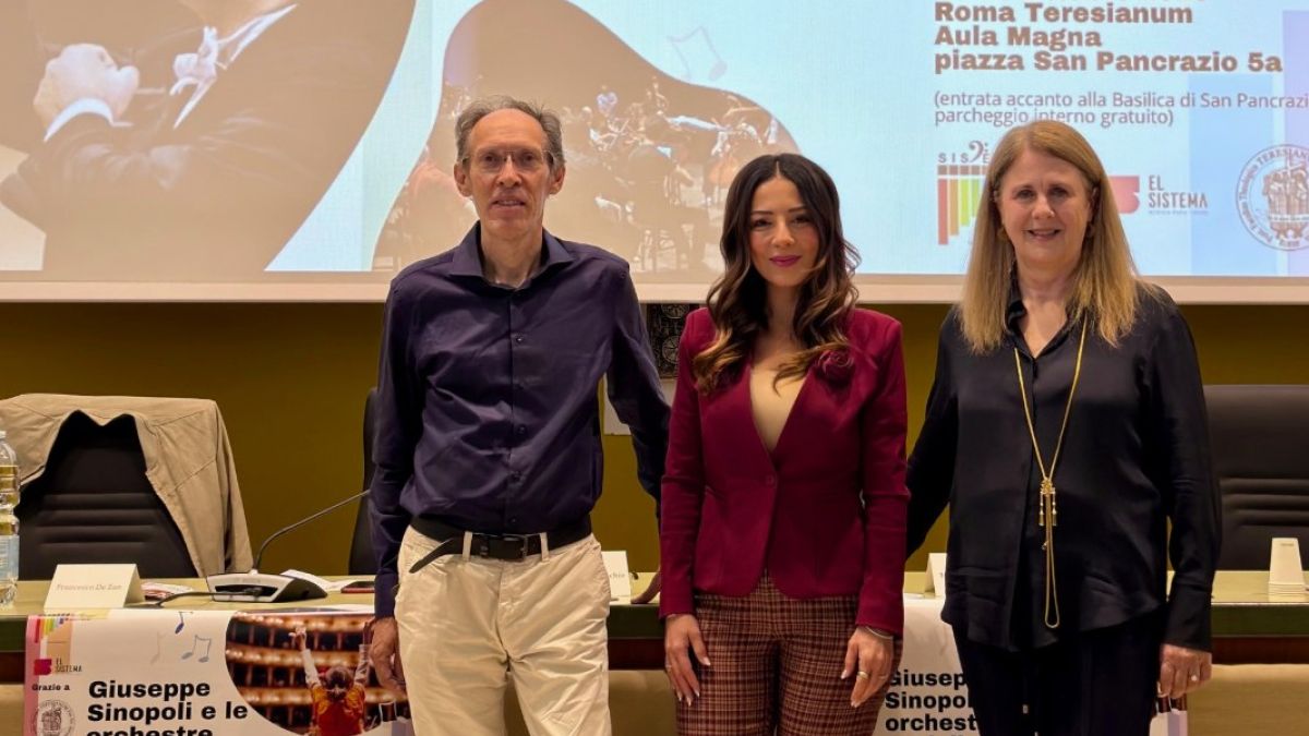 Tres personas posan de pie frente a una pantalla en un auditorio