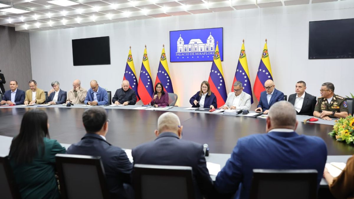 Personas reunidas en torno a una mesa, frente a banderas de Venezuela y una pantalla con el texto «Palacio de Miraflores»