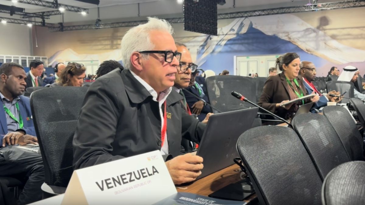 Un delegado sentado ante una computadora portátil, detrás de un letrero de Venezuela, en una sala de conferencias