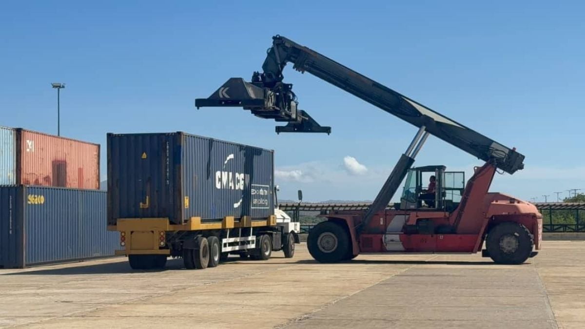 Una grúa portacontenedores junto a un camión que lleva un contenedor en un patio de carga