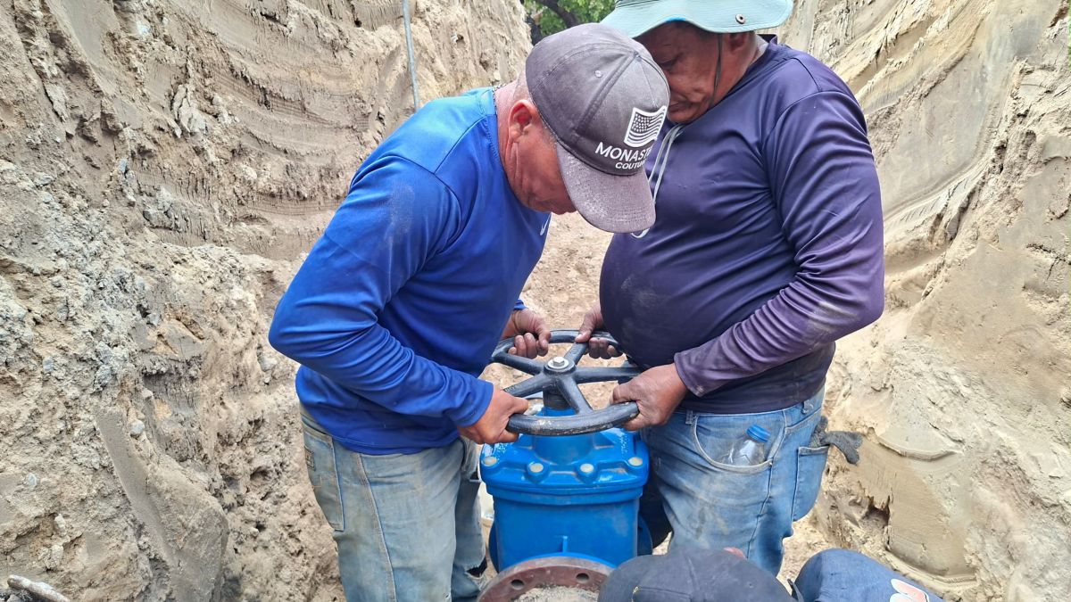 Dos trabajadores giran la manivela de una válvula azul dentro de una zanja