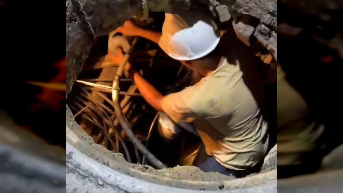 Un trabajador con casco revisa cables dentro de una tanquilla