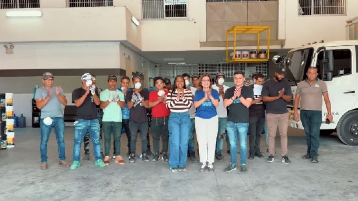 Un grupo de personas aplaude frente a un depósito, junto a un camión